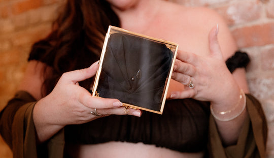 Person holding a small rectangular mirror with a black interior, showing a small object on their arm.